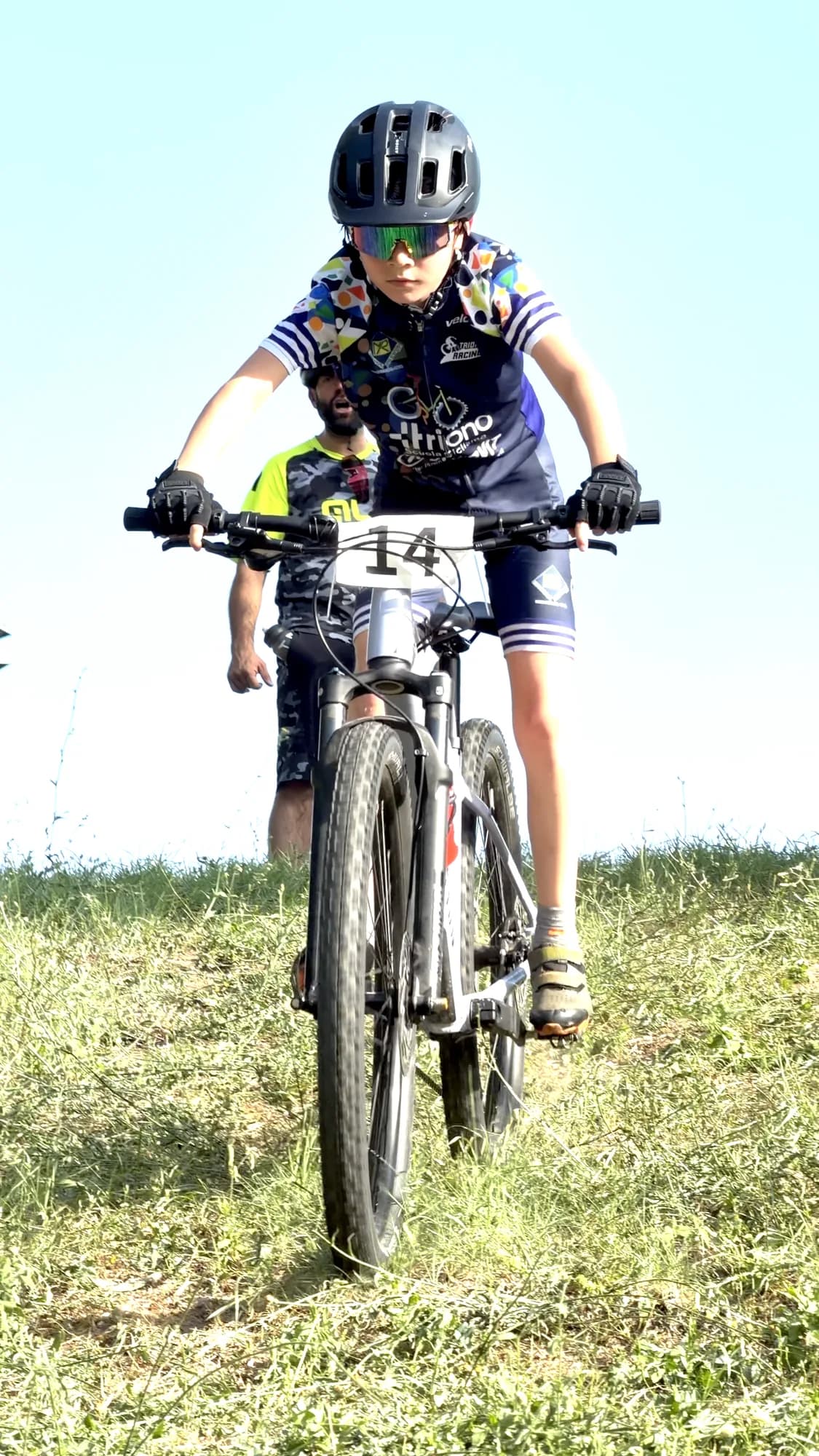 Giovane atleta Triono in mountain bike arriva in cima al prato, il maestro alle sue spalle