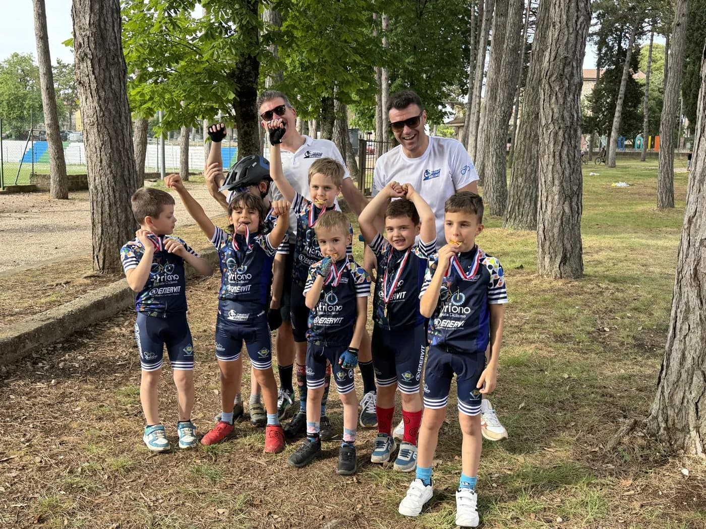 Giovani atleti della Scuola Triono mordono la medaglia dopo la gara, due maestri esultano dietro di loro