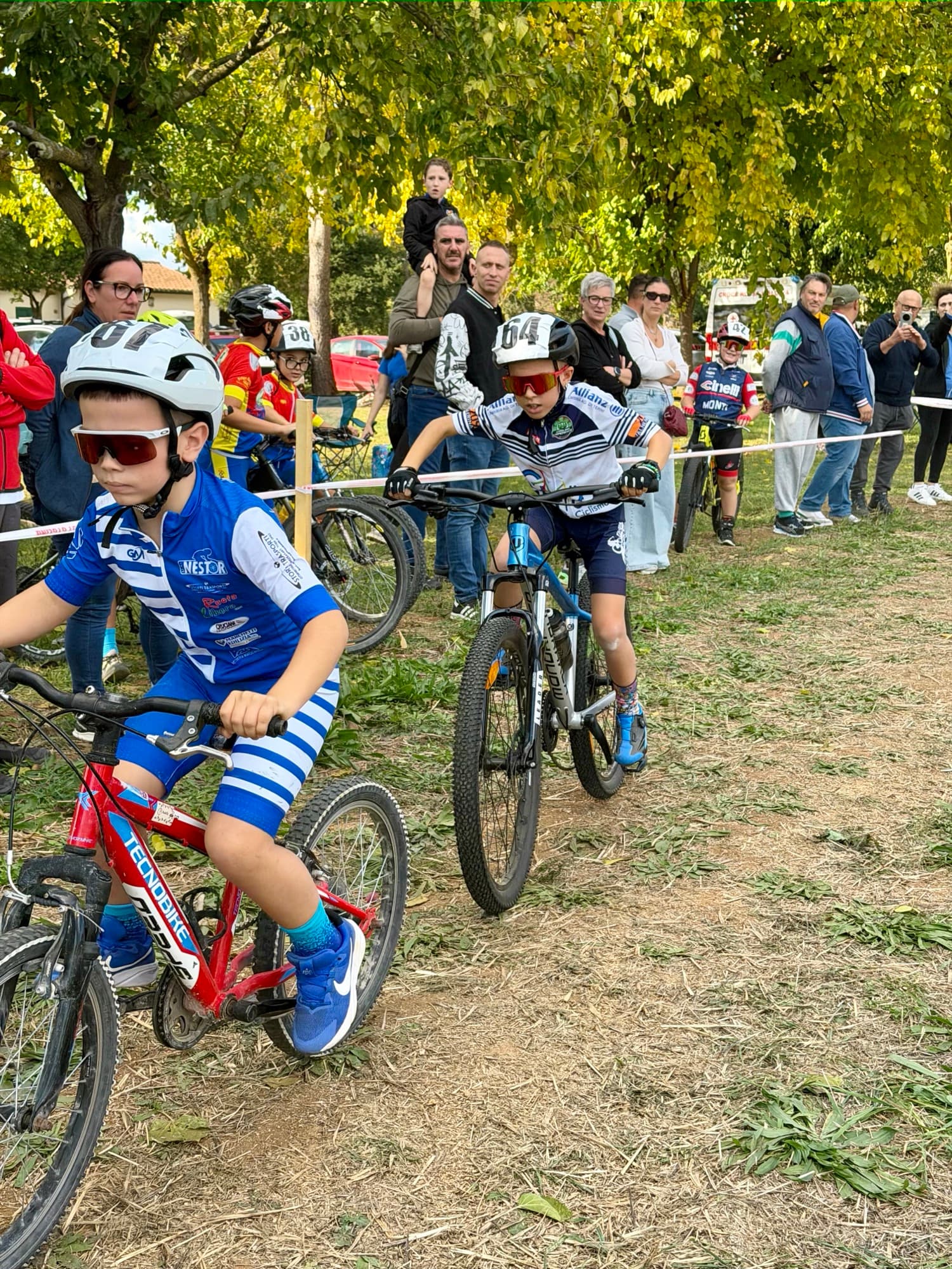 Partenza di una gara di cross country giovanile: piccoli atleti su mountain bike e pubblico a bordo percorso