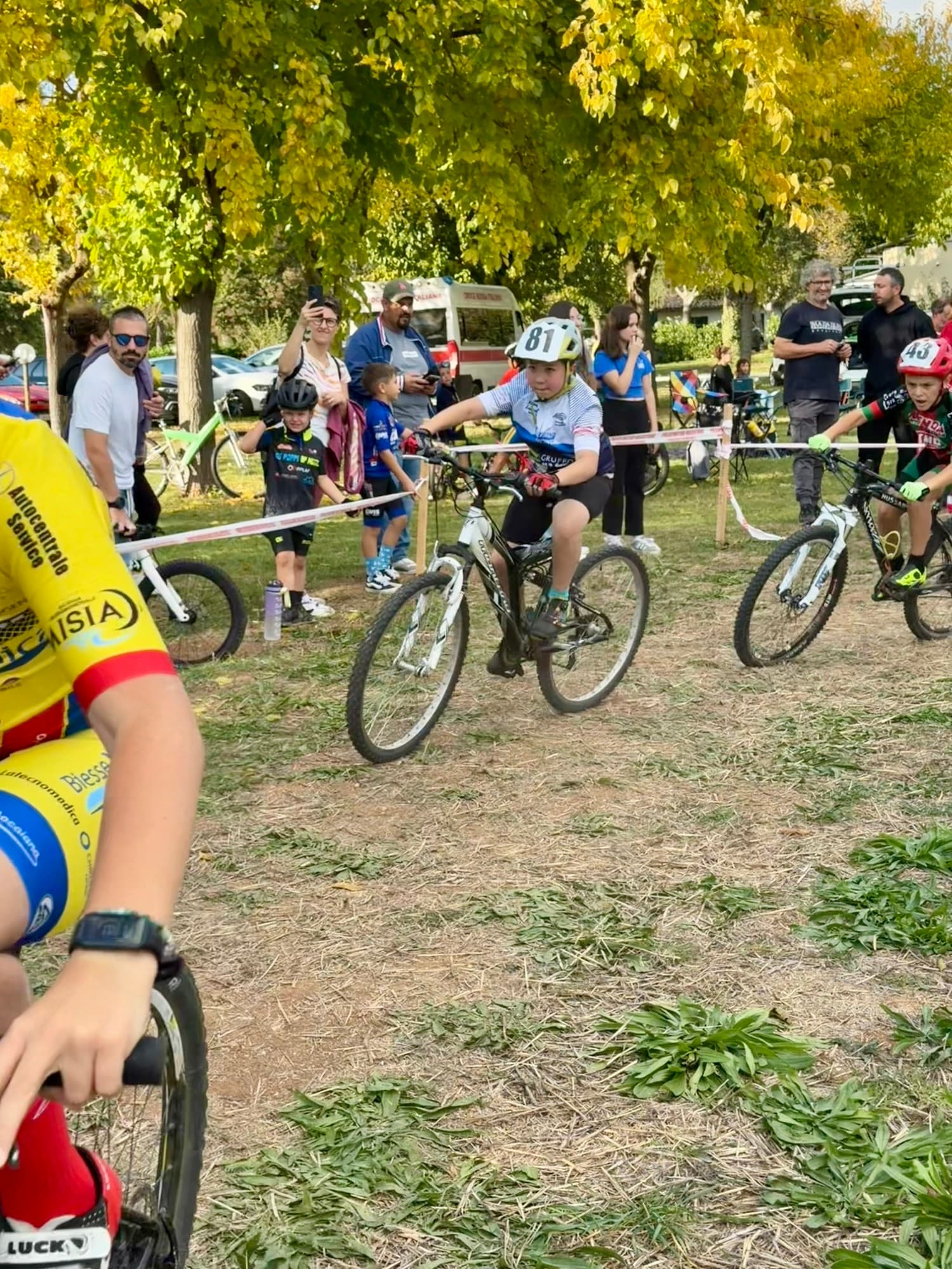 Bambini schierati alla partenza di una gara giovanile su prato, genitori e pubblico intorno