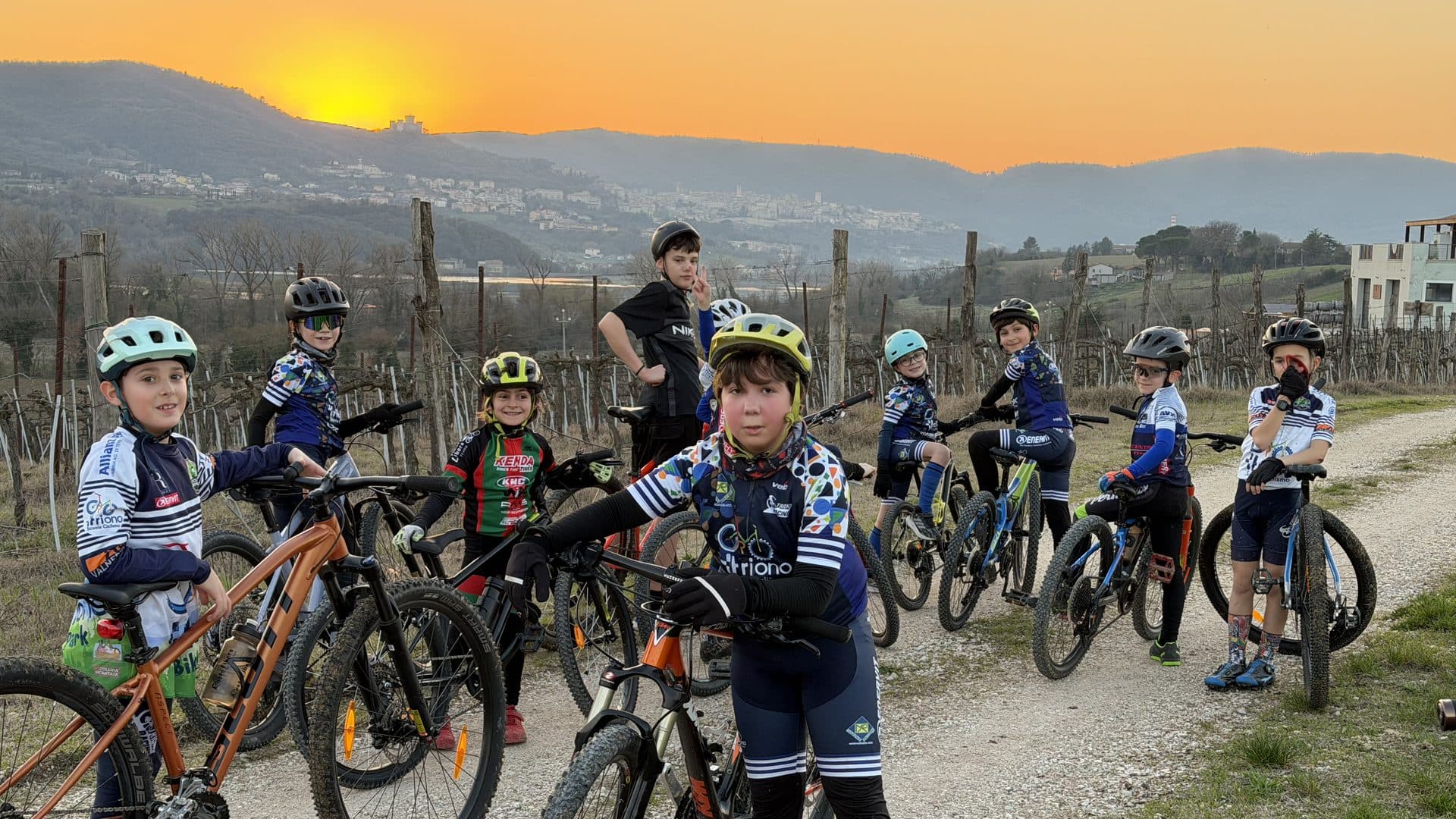 Gruppo di bambini della Scuola Triono al ciclodromo, in maglia ufficiale, paesaggio collinare al tramonto