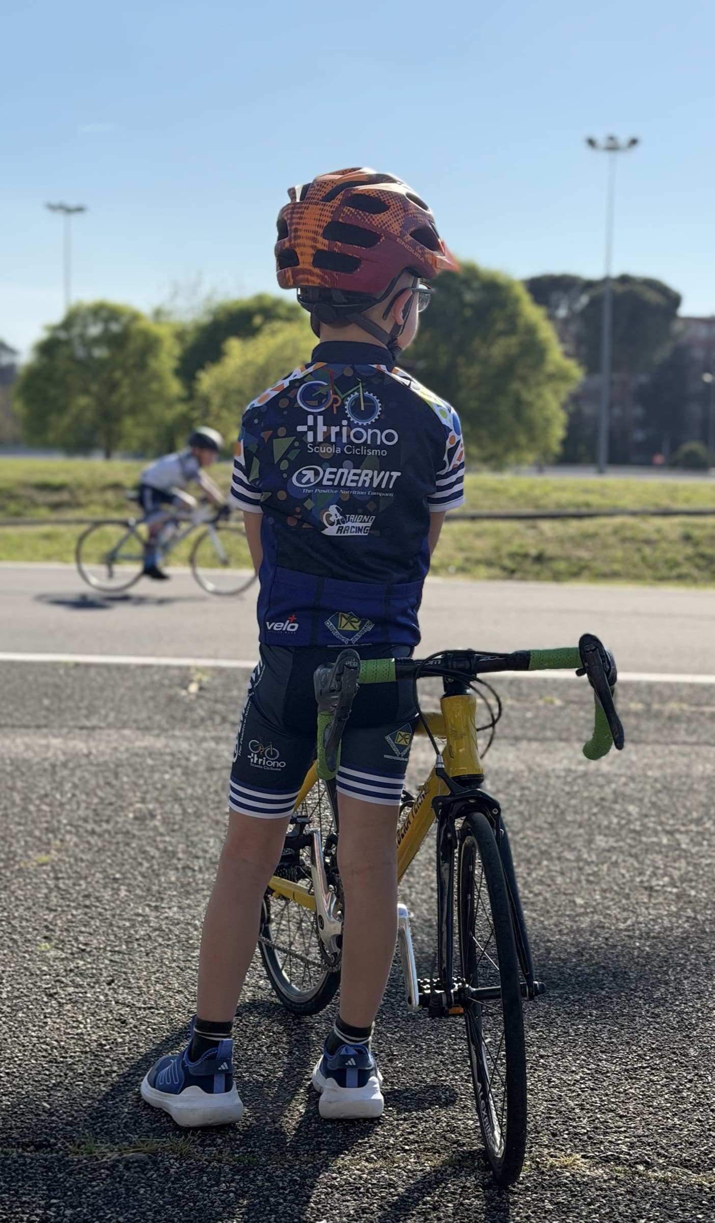 Un bambino della scuola, di spalle e col casco allacciato, fermo accanto alla sua bici prima di partire.