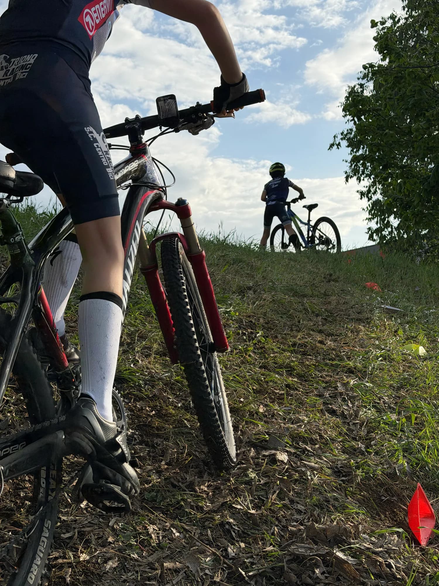 Due allievi in mountain bike affrontano una salita sul prato durante la lezione del giovedì