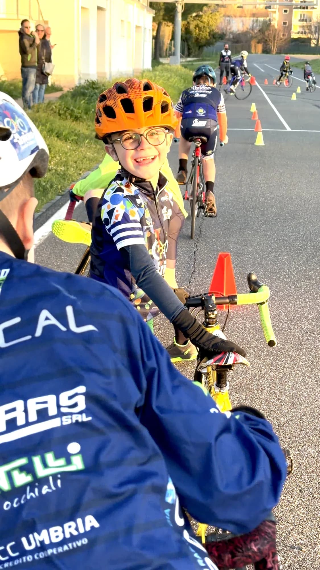 Un allievo della Scuola Triono sorride in sella alla bici durante un esercizio tra i coni, al tramonto